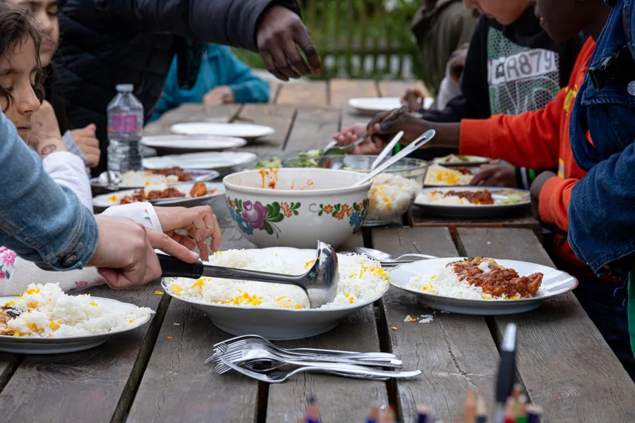 Kinder und Erwachsene essen gemeinsam an einem langen Holztisch im Freien